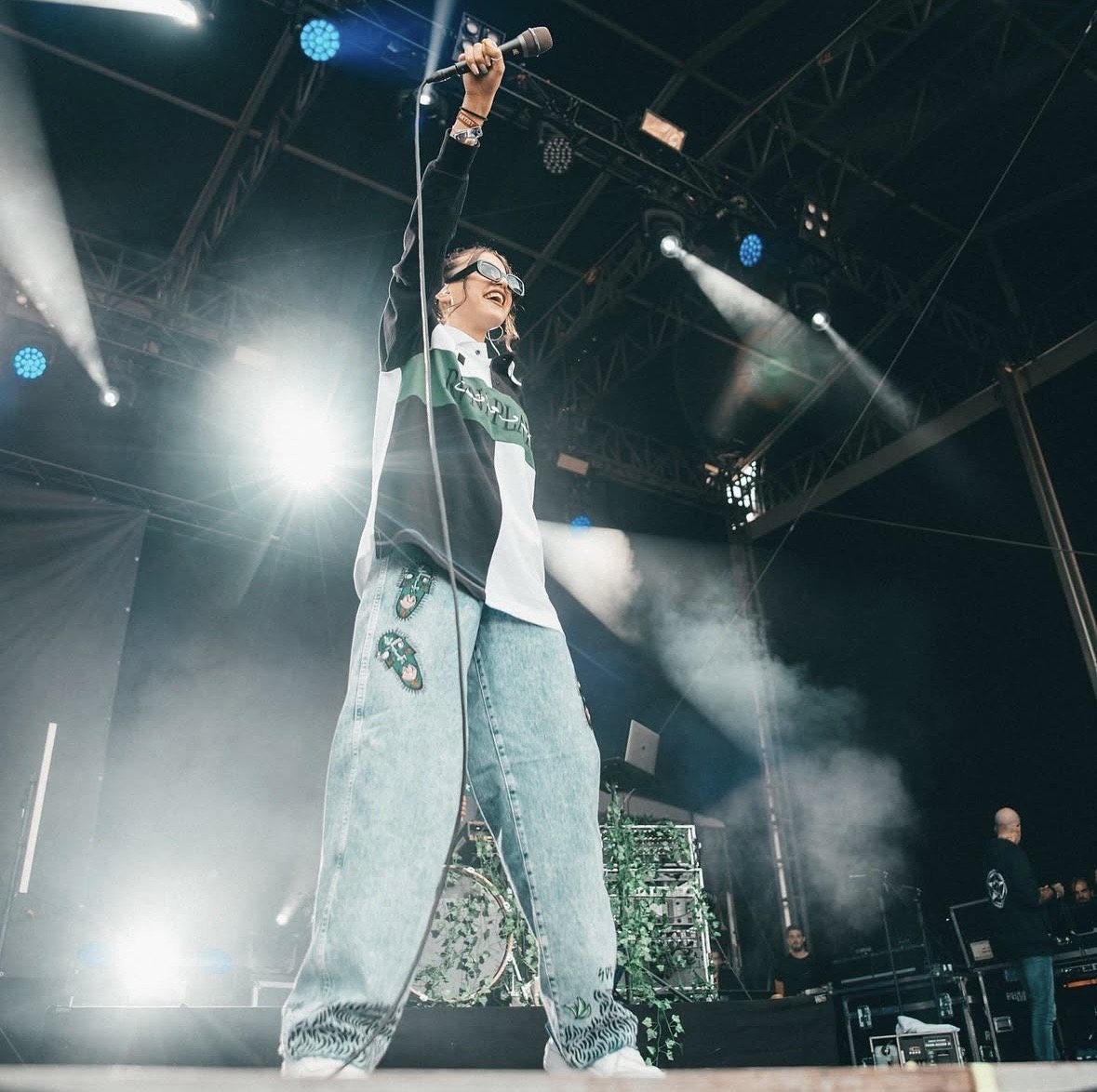 Artist backlit with arm raised on a festival stage